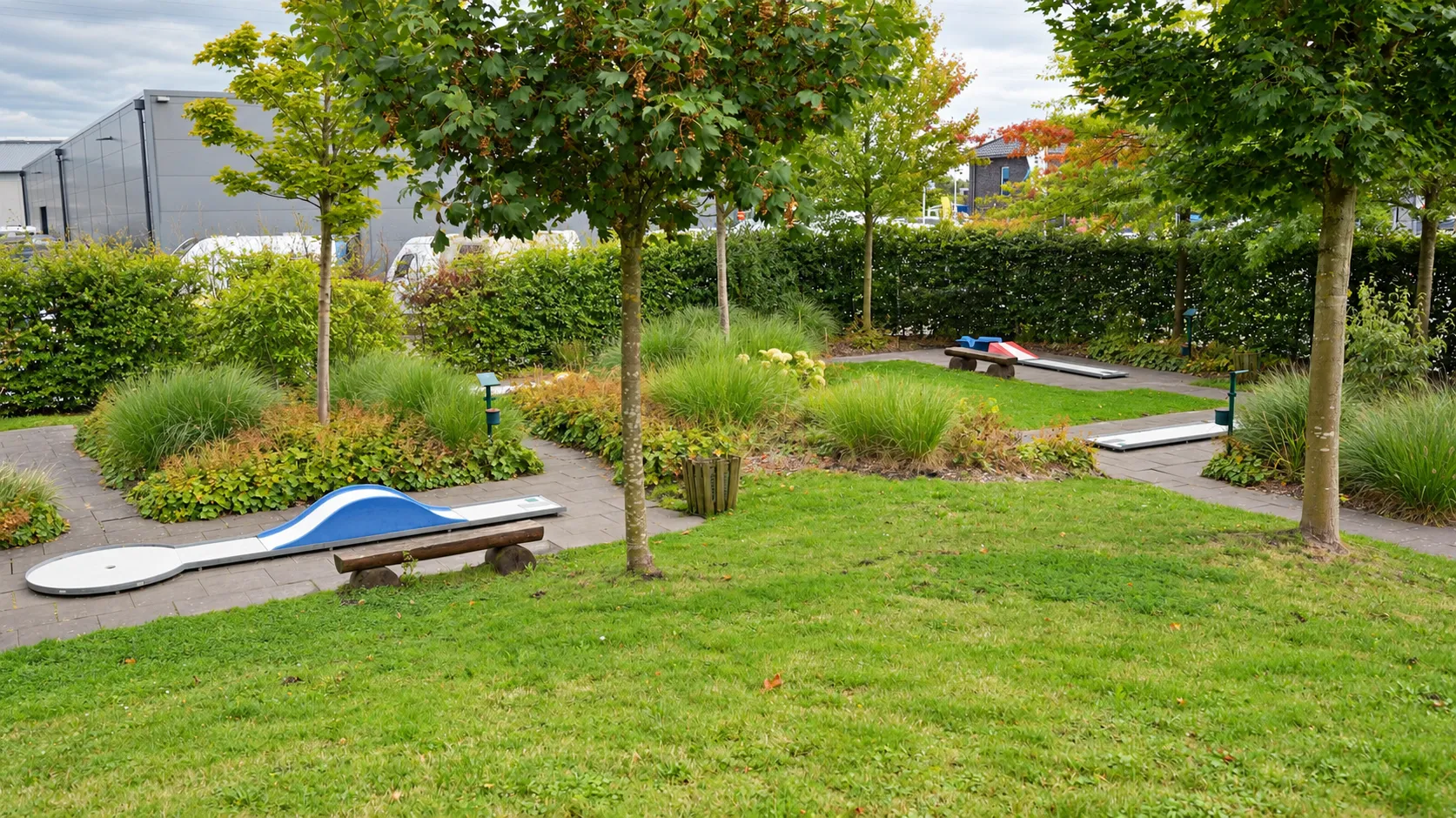Blick über die Minigolfanlage mit mehreren Bahnen zwischen Hecken und Bäumen