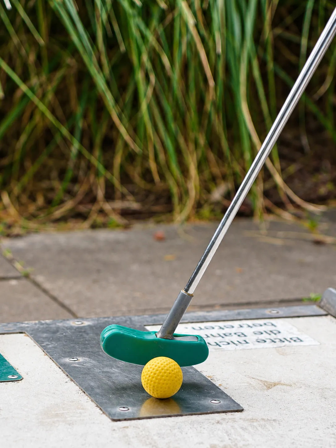 Schläger und gelber Ball auf dem Abschlag, dahinter hohes Gras